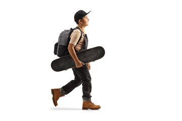 Wall Mural - Full length profile shot of a pre-teen boy walking and holding a skateboard