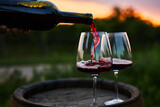 Fototapeta Sypialnia - Pouring red wine into glasses on the barrel at dusk