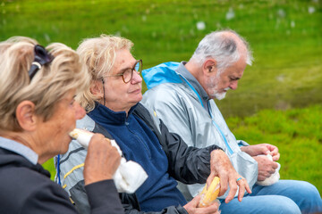 Poster - Elderly people relaxing at the end of a mountain hike, eating sandwiches on the grass.