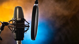 Fototapeta Miasto - Professional studio microphone and pop filter on a beautiful yellow-blue smoky background. Night club, concert, radio broadcasting, television, recording studio, purity of sound, vocals, music.