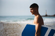 © Cavan Images - Side view of young man holding his surfboard on the beach.