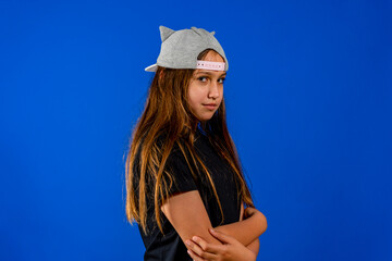 Wall Mural - Picture of angry little girl child standing isolated over blue background. Looking camera with arms crossed