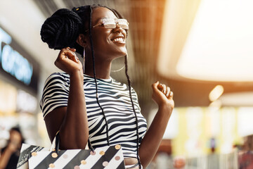 smiling young black woman, holding shopping bags, shopping mall