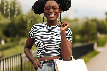 Wall Mural - Young black woman walking outdoors with shopping bags after shopping