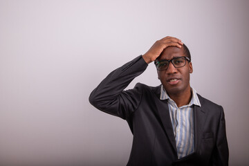 African businessman has a confused expression, he puts his hand on his head and is disoriented. Man with eyeglasses and lost expression, copy space on the person's left