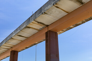 Wall Mural - Concrete roadway on a single central support seen from underneath, isolated against blue sky, horizontal aspect