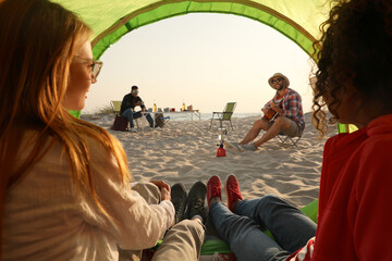 Wall Mural - Friends resting on sandy beach. View from camping tent