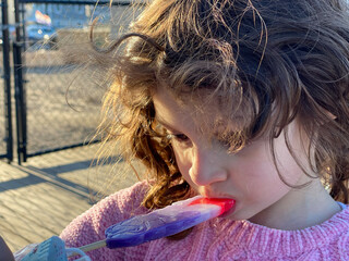 Wall Mural - young girl eating an ice rainbow-colored pop on a summer day