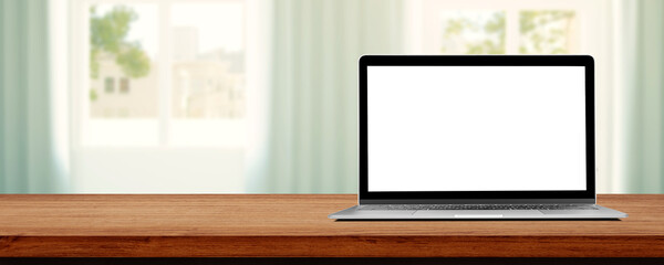 Laptop with blank white screen on wooden table and blurry image of Living room in background.