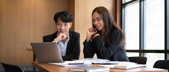 two young business people discussing financial data on computer laptop together in office.