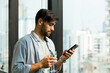 © amorn - Business man using mobile phone near window at work. Man using smartphone near window in the office
