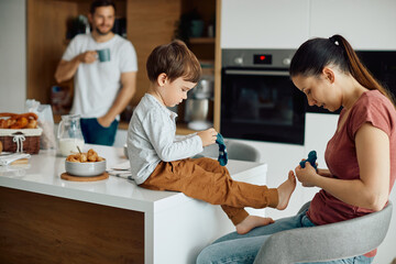 Wall Mural - Young mother assists her son in dressing up his socks at home.