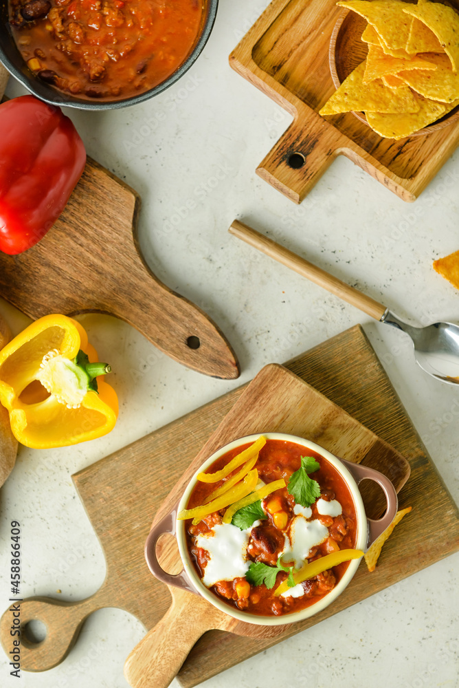 Pot with delicious chili con carne, pepper and nachos on light background
