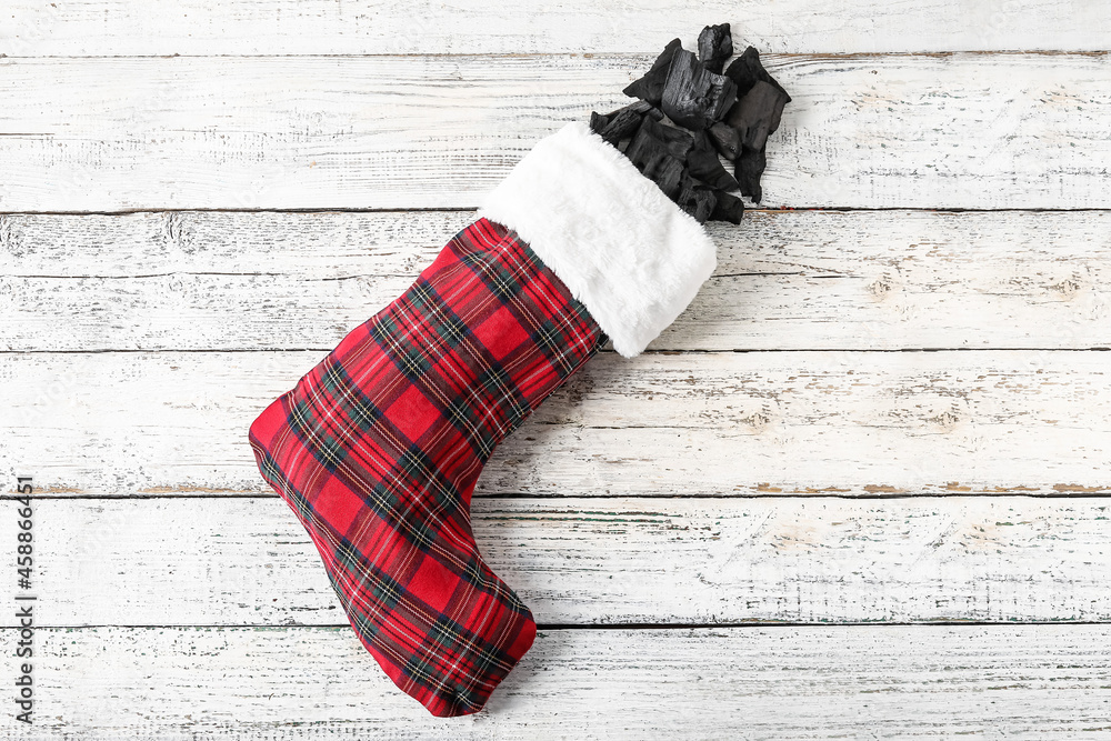 Christmas sock with coal on white wooden background