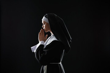 Wall Mural - Young praying nun on dark background