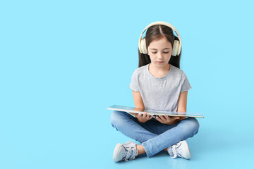 Canvas Print - Little girl with headphones and book on color background