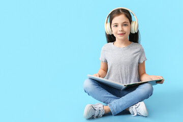 Little girl with headphones and book on color background