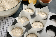 Baking tin with uncooked muffins and poppy seeds on table