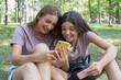 © hannamartysheva - Mom and teenage daughter take a walk in the summer park. Using a smartphone