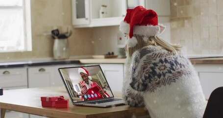 Canvas Print - Animation of snow falling over happy caucasian woman in santa hat on laptop video call