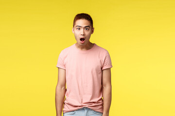 People, different emotions and lifestyle concept. Portrait of astounded, shocked asian male student in awe, drop jaw and gasping speechless, standing startled over yellow background amused