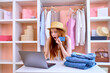 © alfa27 - Woman with credit card using laptop for online shopping to buy new clothes sitting behind table, after wardrobe decluttering, in shock by prices. E-commerce concept. Sell second-hand clothes online
