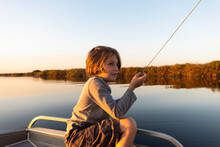 Young Boy Fishing From A Boat On The Okavango Delta At Sunset, Botswana.