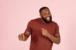 © sergiymolchenko - Positive bearded African-American guy actor in brown t-shirt dances standing on light pink background in studio close view