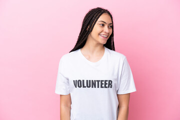 Poster - Teenager volunteer girl with braids isolated on pink background looking side