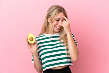 Poster - Young caucasian woman holding an avocado isolated on pink background laughing