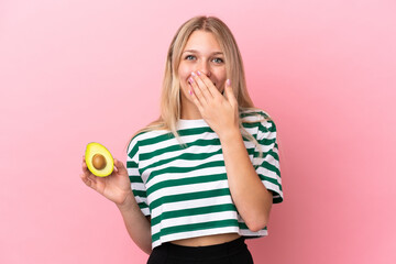 Poster - Young caucasian woman holding an avocado isolated on pink background happy and smiling covering mouth with hand