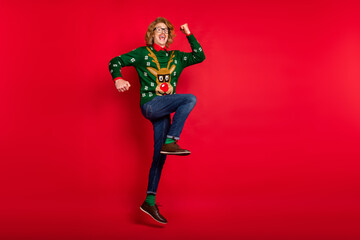 Poster - Photo of funny lucky young guy dressed print pullover smiling jumping rising arms empty space isolated red color background