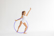 slim artistic teenager girl in white leotard trains on white background with hoop in her hands in rhythmic gymnastic exercise, children's professional sports