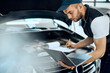 © Drazen - Car mechanic uses laptop and writes data during engine maintenance at auto repair shop.