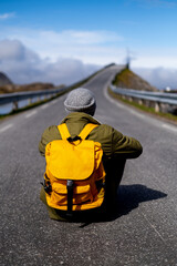 Fototapete - Guy travels with a yellow backpack through picturesque places with beautiful mountain landscapes.