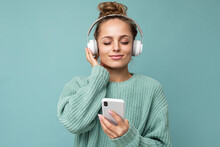 Photo Shot Of Beautiful Joyful Smiling Young Female Person Wearing Stylish Casual Outfit Isolated Over Colorful Background Wall Wearing White Bluetooth Wireless Earphones And Listening To Music And