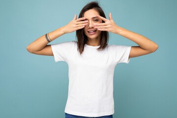 Photo of young positive happy smiling beautiful woman with sincere emotions wearing stylish clothes isolated over background with copy space and hiding with hands