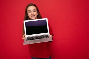 Photo of beautiful young girl holding computer laptop looking at camera isolated over colourful background