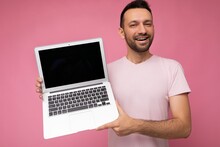 Handsome Man Holding Laptop Computer Looking At Camera In T-shirt On Isolated Pink Background
