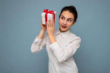 Shot of attractive positive smiling young brunette woman isolated over colourful background wall wearing everyday trendy outfit holding gift box and looking to the side