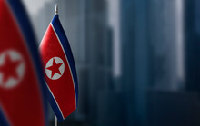 Small Flags Of North Korea On A Blurry Background Of The City