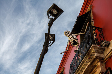 Wall Mural - Low-angle shot of a creepy skeleton on the balcony of a red building on a spooky season