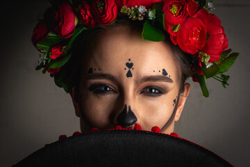 Wall Mural - young girl with scarecrows makeup for the Day of the Dead with a wreath of flowers on his head, in a network with flowers scarf covered his face sambrero and looks black hat. Halloween or La Calavera 