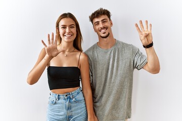 Sticker - Young beautiful couple standing together over isolated background showing and pointing up with fingers number nine while smiling confident and happy.