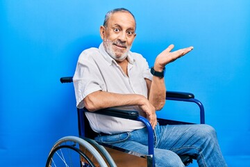 Sticker - Handsome senior man with beard sitting on wheelchair smiling cheerful presenting and pointing with palm of hand looking at the camera.