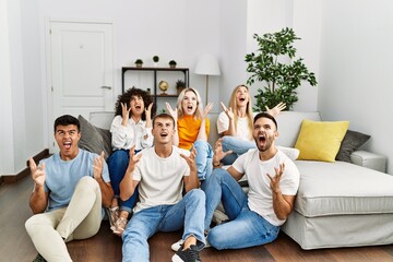 Sticker - Group of people sitting on the sofa and floor at home crazy and mad shouting and yelling with aggressive expression and arms raised. frustration concept.