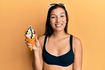 Poster - Young latin woman wearing bikini holding ice cream looking positive and happy standing and smiling with a confident smile showing teeth