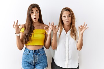 Poster - Mother and daughter together standing together over isolated background looking surprised and shocked doing ok approval symbol with fingers. crazy expression