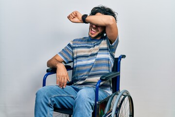 Sticker - Handsome hispanic man sitting on wheelchair covering eyes with arm smiling cheerful and funny. blind concept.