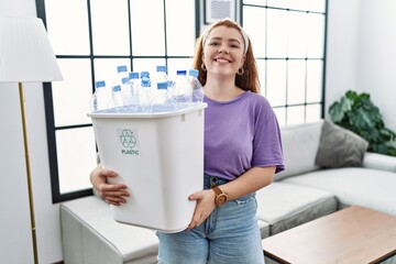 Sticker - Young redhead woman holding recycling wastebasket with plastic bottles with a happy and cool smile on face. lucky person.